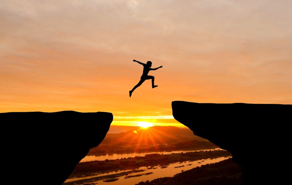 man jumping over cliff on sunset background