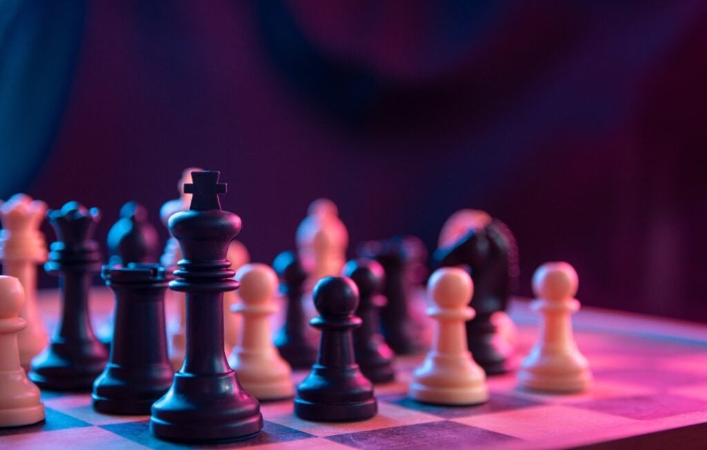 Chess pieces on a chessboard on a dark background shot in neon pink-blue colors.