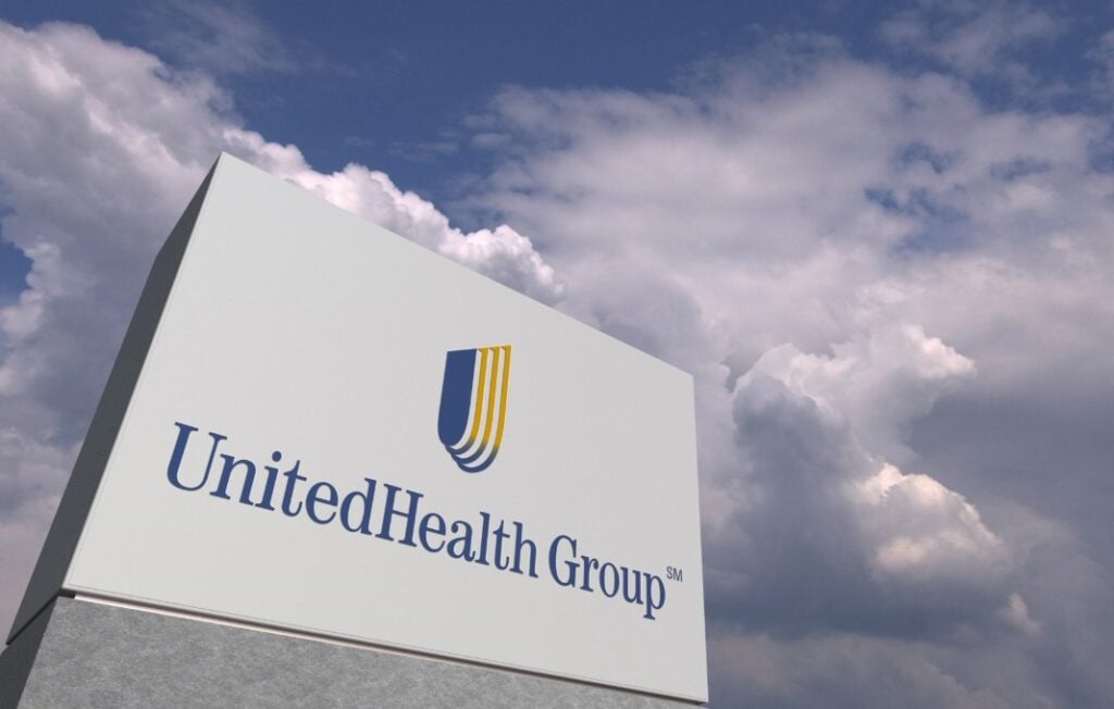 Logo of UNITEDHEALTH GROUP on a stand against cloudy sky, editorial 3D rendering
