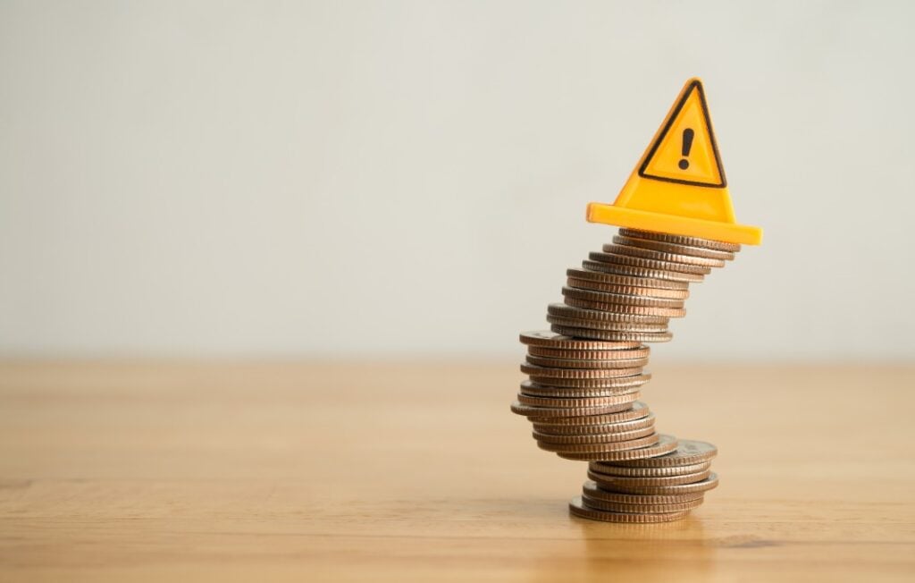 Warning sign label on stack coins in uncertainty situation on wooden table with white background