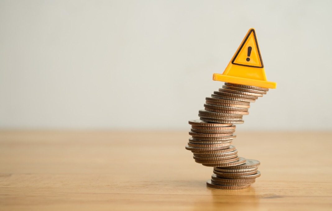Warning sign label on stack coins in uncertainty situation on wooden table with white background