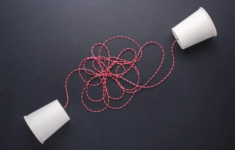Two white paper cup connect with red rope used for classic phone on black stone table board.