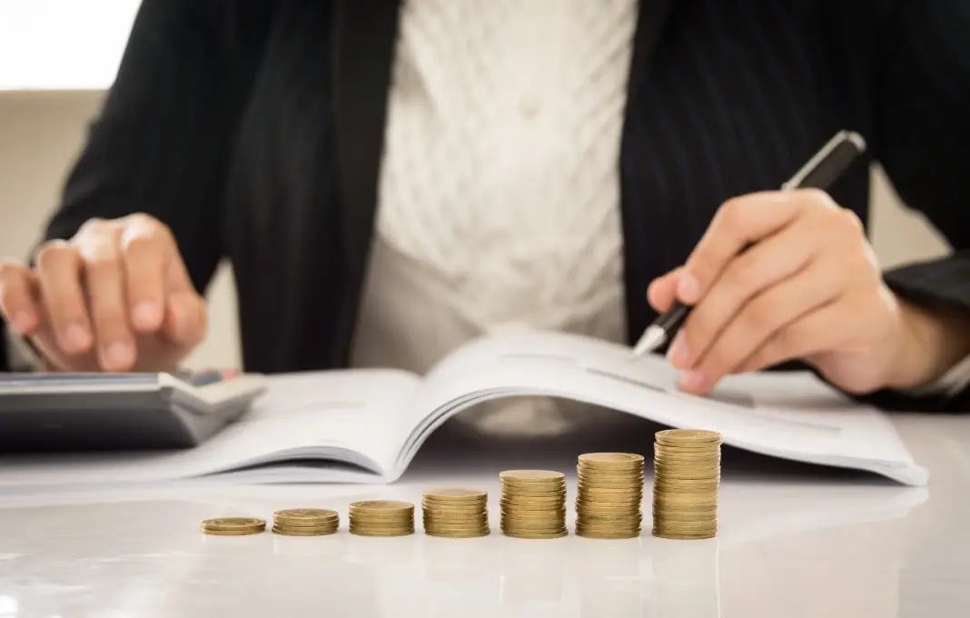 Ascending stacks of coins in the foreground of someone writing in a notebook