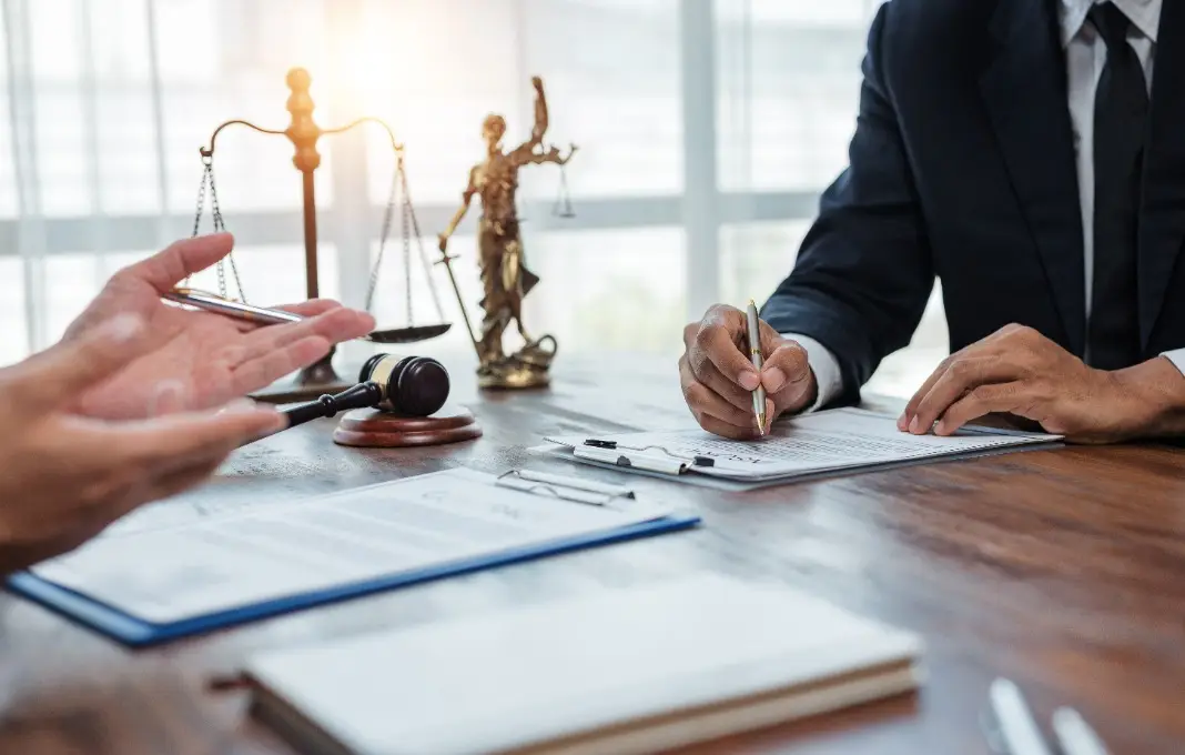 Lawyer and client discussing terms and conditions while signing legal document in office with gavel and justice scales in background