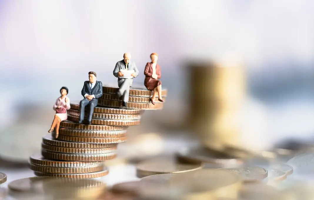 Miniature people sitting on coins stack.