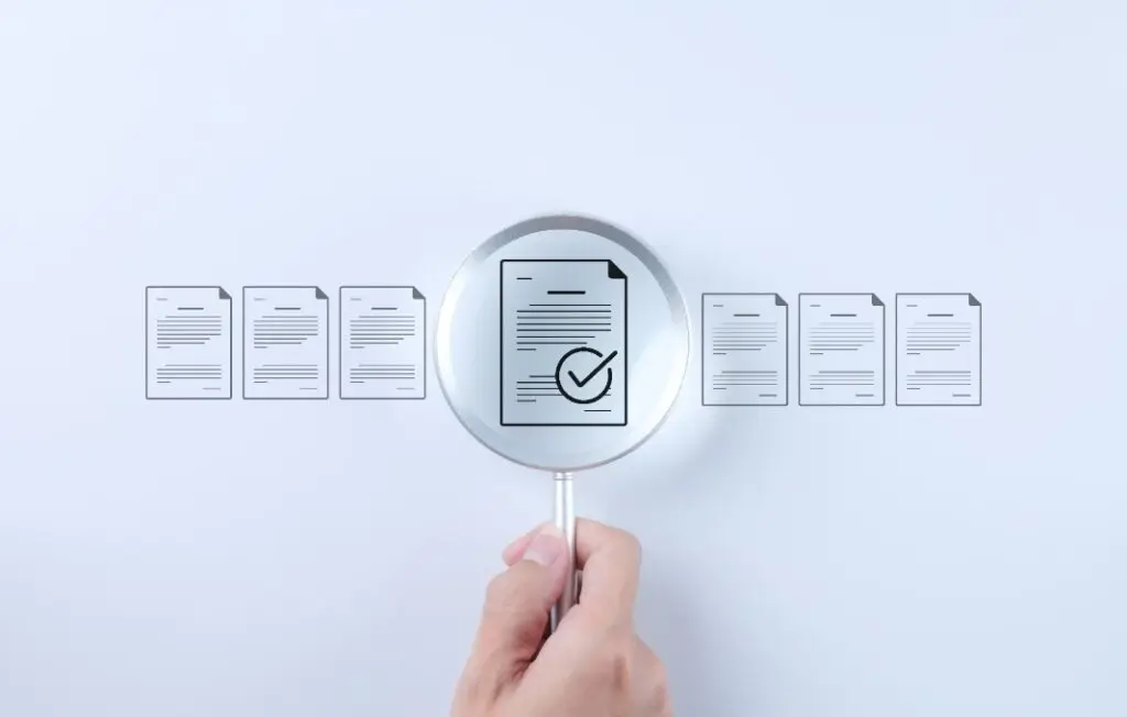 Hand holding magnifying glass over icon of sheet of paper